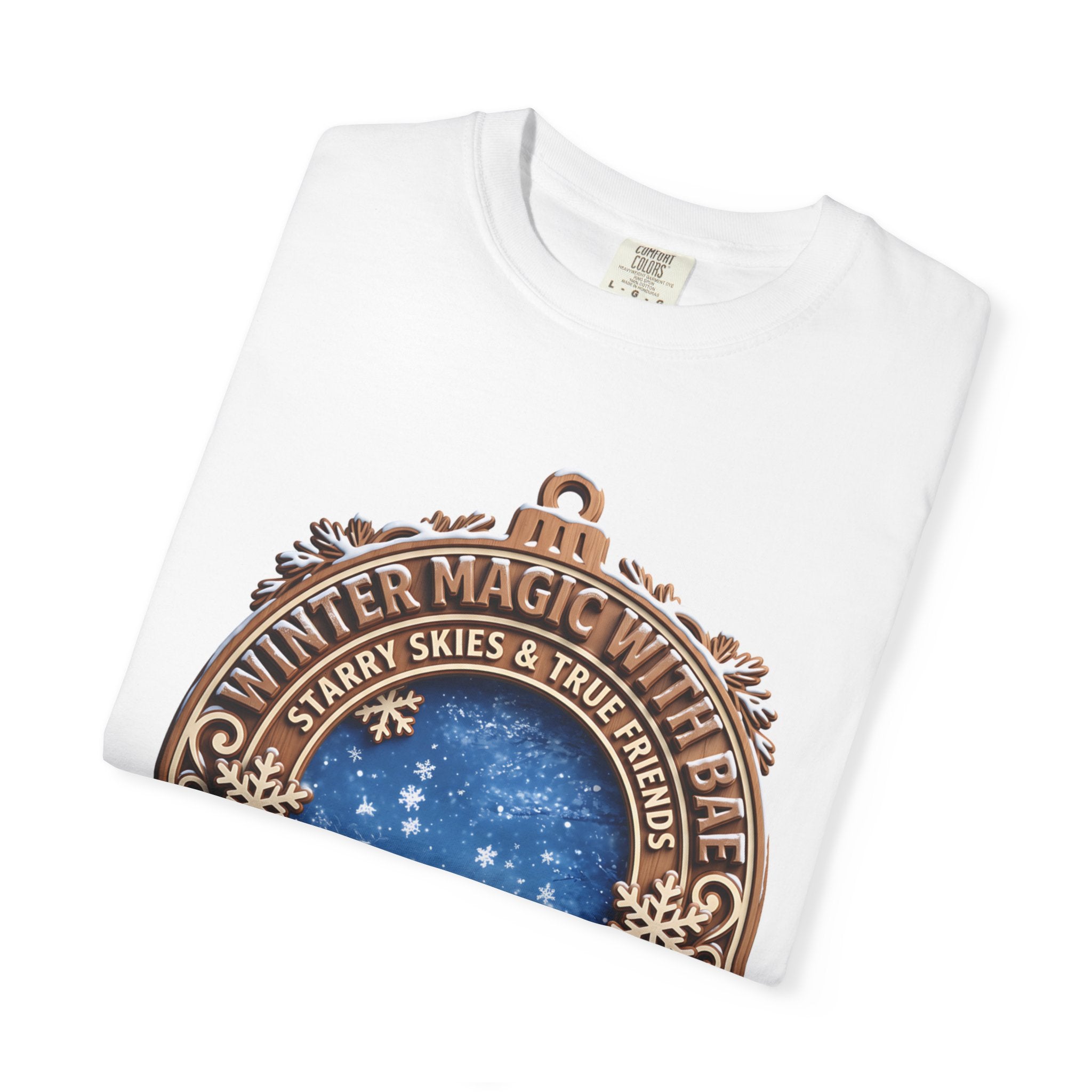 Folded white t-shirt showing the top of the Winter Magic With Bae badge and its snowflake border